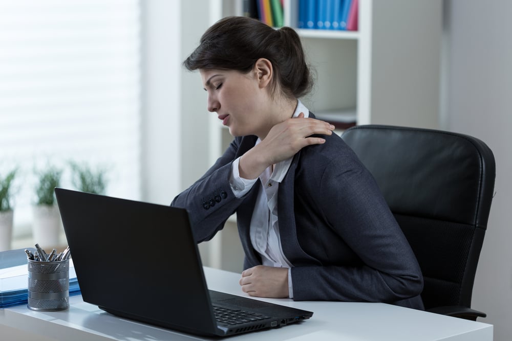 Woman at her desk rubbing her stiff neck and jaw